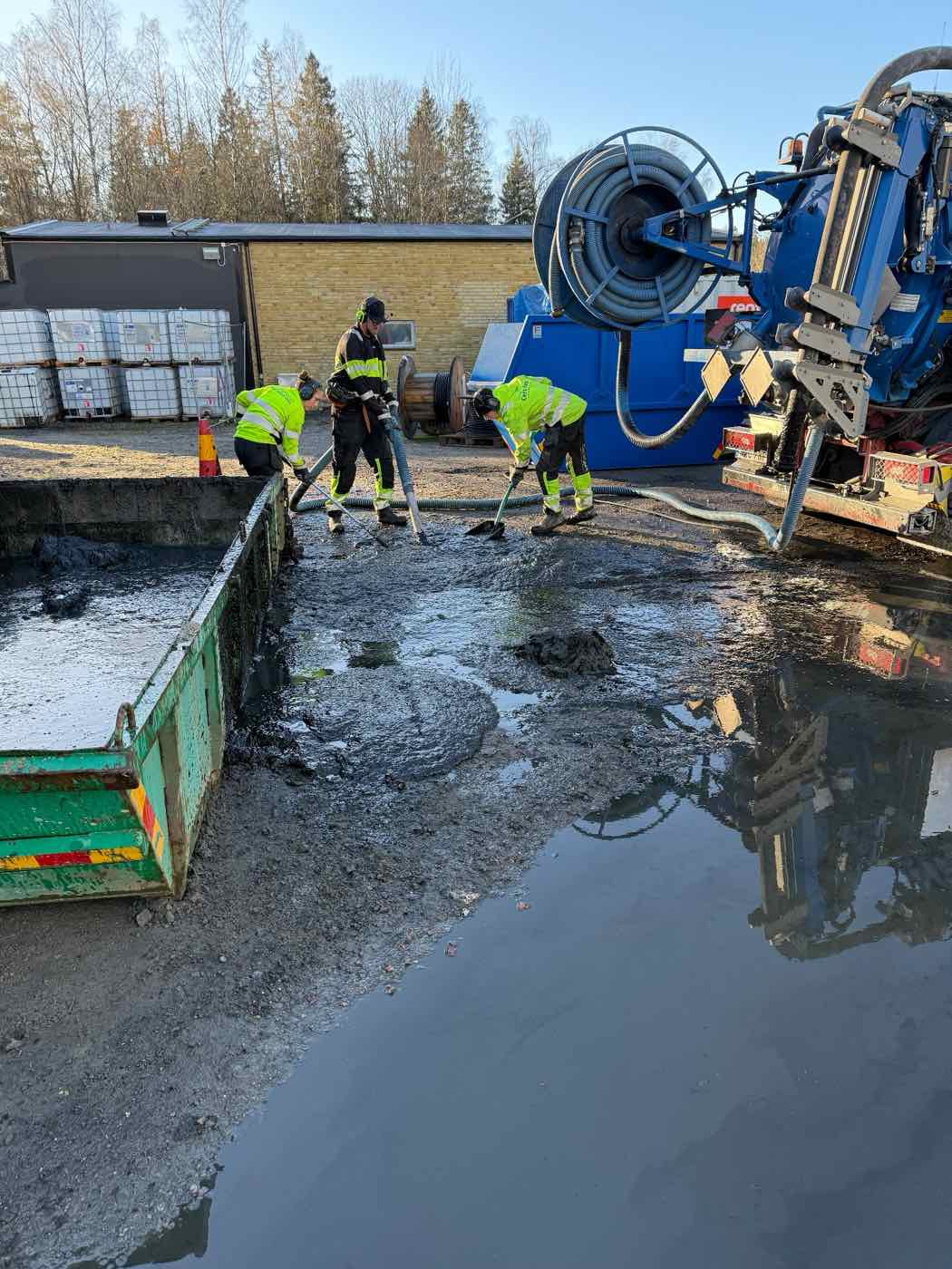 Personal i varselkläder arbetar med slamsugning vid en container